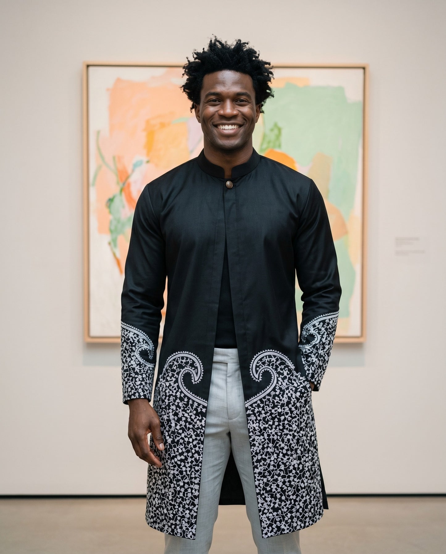 Man wearing a black and white patterned coat standing in front of abstract paintings.