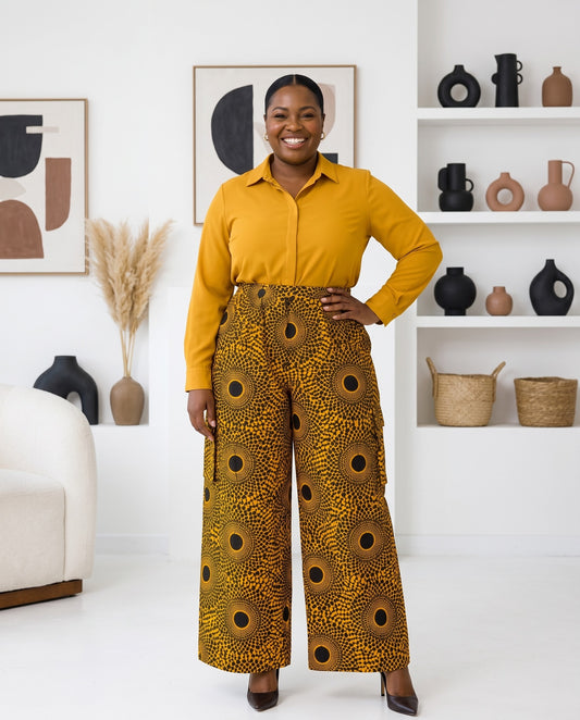 Woman wearing a yellow shirt and patterned pants standing in a room with decorative items on shelves.