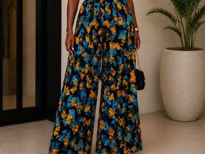 Woman wearing a black top and blue and yellow floral skirt standing indoors with a plant in the background.