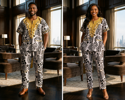 A man wearing a matching two-piece tunic and trouser set with a bold black, white, and gold abstract pattern, standing in a modern, upscale living room with large windows and brown leather armchairs.