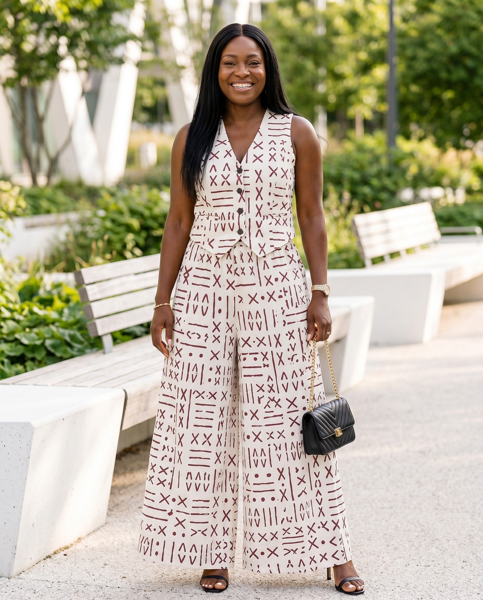 Woman in a patterned dress standing outdoors with greenery and benches in the background
