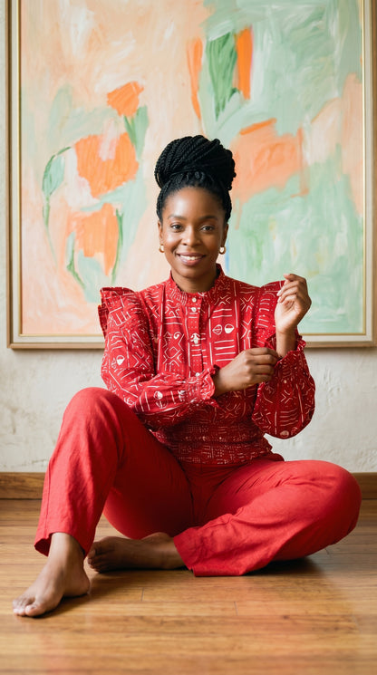 Woman in a red outfit sitting on the floor in front of a colorful abstract painting.