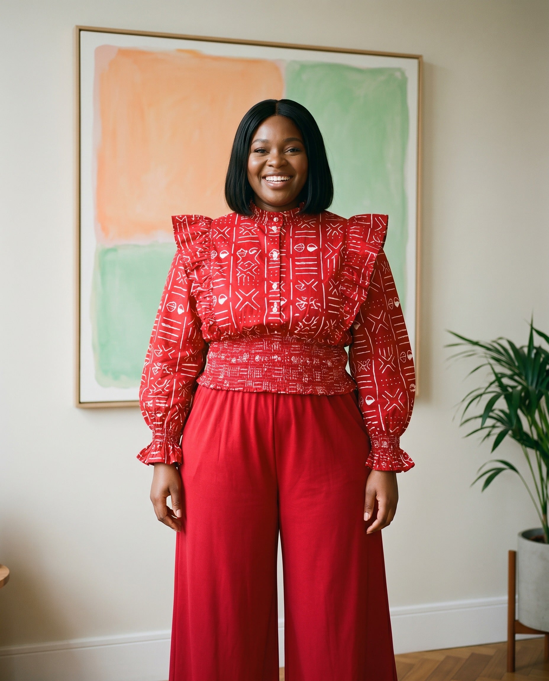 Woman wearing a red patterned top and red pants standing in a room with a colorful abstract painting on the wall.