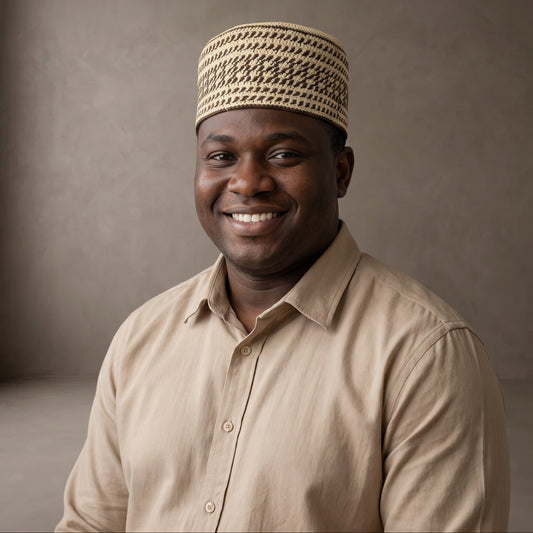 A smiling man wearing a beige button-up shirt and a beige patterned knit skullcap, photographed against a plain textured gray studio background.