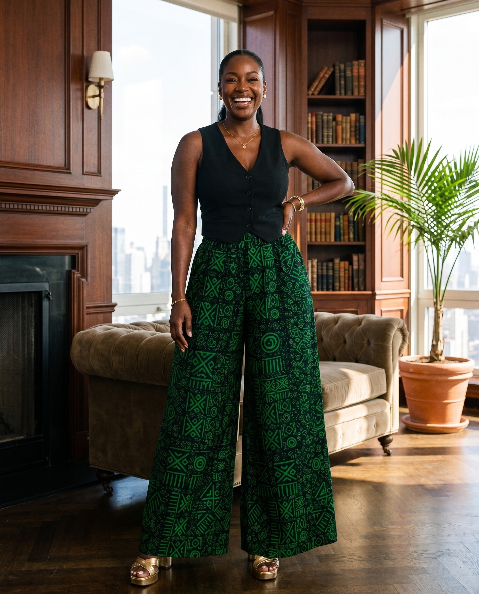 Woman in a black top and green patterned pants standing in a room with bookshelves and a plant.