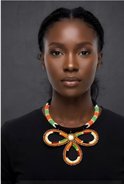 A woman wearing a large, colorful beaded bow-shaped necklace with green, orange, and white beads over a black top, set against a dark gray background.