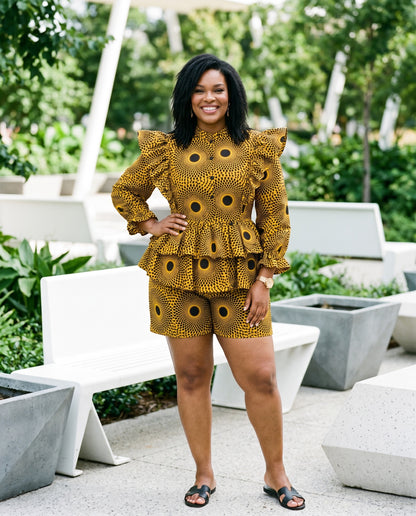 Woman in a yellow patterned outfit standing outdoors with greenery in the background